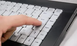 Palec naciska klawisz Enter na klawiaturze laptopa, co może być częścią instrukcji, jak zablokować program w firewall.