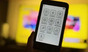 Dłoń trzyma smartfon z ikonami aplikacji: aparat, dyktafon, e-czytnik, kalkulator, mapy, medytacja, muzyka, notatki, pogoda, szachy. To komunikator bez numeru telefonu.