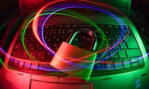 Kłódka na klawiaturze laptopa, otoczona kolorowymi smugami światła, symbolizuje bezpieczeństwo i ochronę danych. Dostępny darmowy antywirus zapewni Ci spokój.