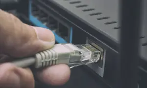 Dłoń podłącza kabel sieciowy kategorii do routera, zapewniając stabilne połączenie internetowe.