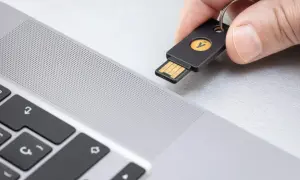 Dłoń zbliża klucz U2F do laptopa. To proste rozwiązanie, które odpowiada na pytanie klucz u2f co to jest – fizyczny klucz do bezpiecznego logowania.