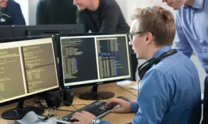 Programiści pracują nad kodem na monitorach, tworząc wolne oprogramowanie.