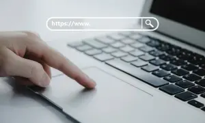 Dłoń na touchpadzie laptopa, pasek adresu z "https://www.", symbol lupy. Bezpieczna poczta online.