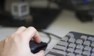 Dłoń steruje myszką na tle klawiatury i monitora. Użytkownik pracuje na systemie Linux, eksplorując jego możliwości.