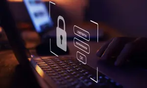 Dłoń wpisuje dane logowania na laptopie. Ikona kłódki symbolizuje bezpieczeństwo. Dowiedz się, jak sprawdzić czy link jest bezpieczny.
