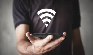 Dłoń trzyma smartfon, nad którym unosi się biały symbol Wi-Fi, symbolizujący szybkie połączenie wi-fi 6e.