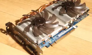 Karta graficzna Gigabyte GTX 560 Ti z dwoma wentylatorami i miedzianymi rurkami cieplnymi na drewnianym tle.