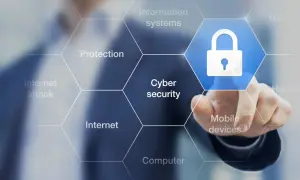 Palec dotyka ikony kłódki, symbolizującej cyberbezpieczeństwo. Wokół widnieją hasła: ochrona, internet, ataki, systemy informatyczne, urządzenia mobilne, komputery. To definicja cyberprzestępczości.