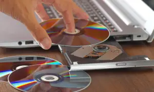 Dłoń wkłada płytę do napędu laptopa, przygotowując się do nagrania danych. Program do wypalania płyt jest kluczowy do archiwizacji.