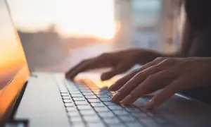 Dłonie piszą na klawiaturze laptopa z systemem MX Linux, w tle zachodzące słońce.