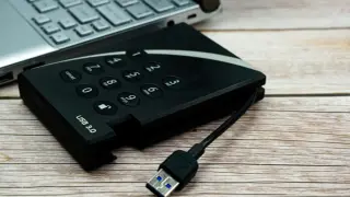Dysk zewnętrzny z klawiaturą numeryczną i kablem USB 3.0 obok laptopa, gotowy do udostępniania internetu z telefonu na komputer przez USB.