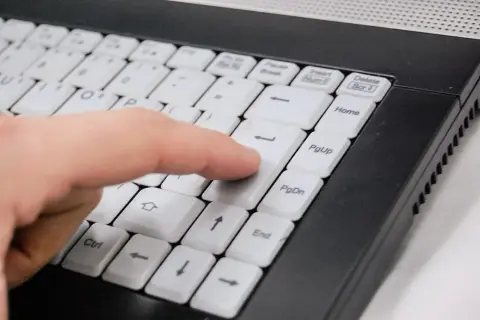 Palec naciska klawisz Enter na klawiaturze laptopa, co może być częścią instrukcji, jak zablokować program w firewall.