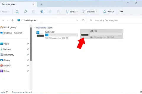 Widok "Ten komputer" z zaznaczonym pendrivem USB (K:). Czerwona strzałka wskazuje na ikonę pendrive'a, sugerując jego szyfrowanie lub przygotowanie do niego.