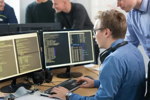 Programiści pracują nad kodem na monitorach, tworząc wolne oprogramowanie.