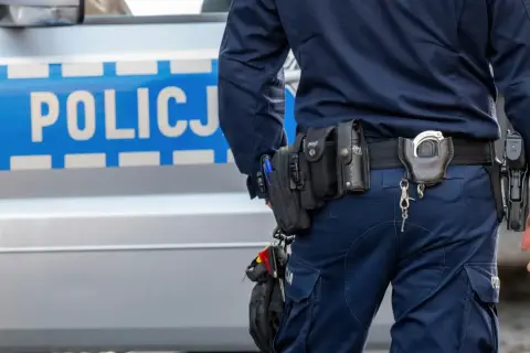 Policjant w pełnym rynsztunku, z pistoletem i kajdankami, stoi obok radiowozu. Wszystko wygląda na rutynową kontrolę, ale czy na pewno? Czasem nawet najbardziej oczywiste sygnały mogą okazać się fałszywym pozytywem.
