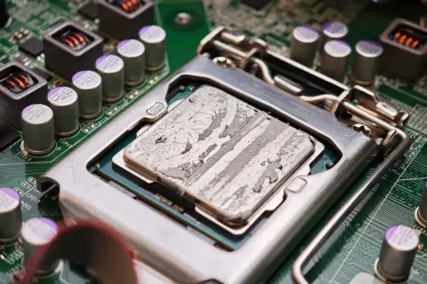 Procesor z zaschniętą pastą termoprzewodzącą, gotowy do testu chłodzenia CPU. Widoczne kondensatory i elementy płyty głównej.