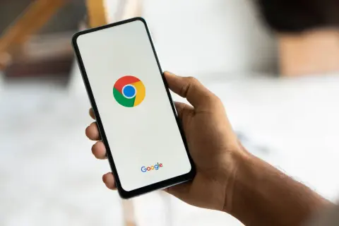 Dłoń trzyma smartfon z logo Chrome. Chcesz wiedzieć, jak usunąć synchronizację Google?