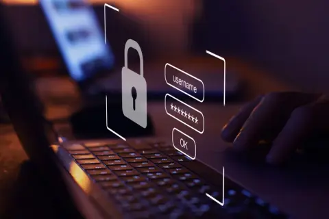 Dłoń wpisuje dane logowania na laptopie. Ikona kłódki symbolizuje bezpieczeństwo. Dowiedz się, jak sprawdzić czy link jest bezpieczny.