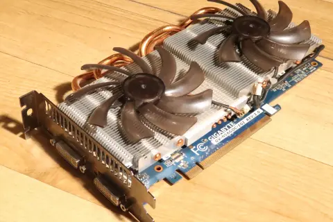 Karta graficzna Gigabyte GTX 560 Ti z dwoma wentylatorami i miedzianymi rurkami cieplnymi na drewnianym tle.