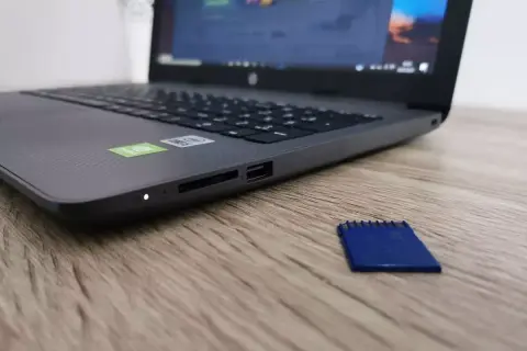 Laptop z czytnikiem kart SD. Obok leży niebieska karta pamięci, która jest zabezpieczona przed zapisem.