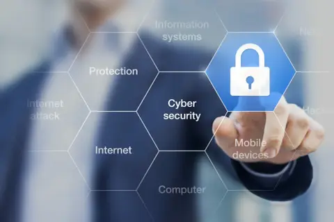 Palec dotyka ikony kłódki, symbolizującej cyberbezpieczeństwo. Wokół widnieją hasła: ochrona, internet, ataki, systemy informatyczne, urządzenia mobilne, komputery. To definicja cyberprzestępczości.