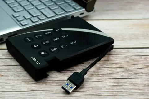 Dysk zewnętrzny z klawiaturą numeryczną i kablem USB 3.0 obok laptopa, gotowy do udostępniania internetu z telefonu na komputer przez USB.