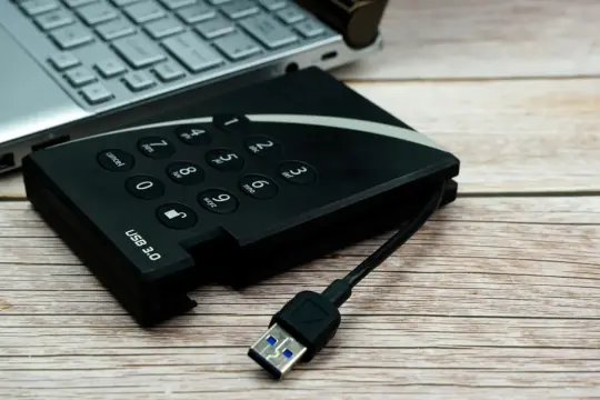 Dysk zewnętrzny z klawiaturą numeryczną i kablem USB 3.0 obok laptopa, gotowy do udostępniania internetu z telefonu na komputer przez USB.