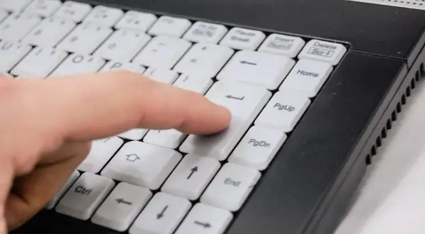 Palec naciska klawisz Enter na klawiaturze laptopa, co może być częścią instrukcji, jak zablokować program w firewall.