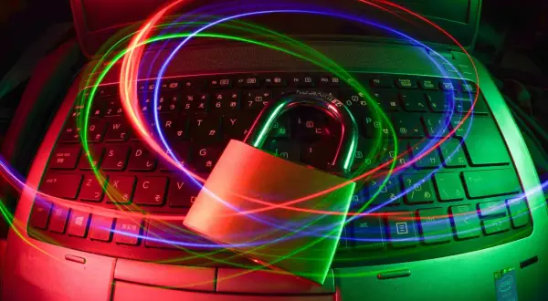 Kłódka na klawiaturze laptopa, otoczona kolorowymi smugami światła, symbolizuje bezpieczeństwo i ochronę danych. Dostępny darmowy antywirus zapewni Ci spokój.