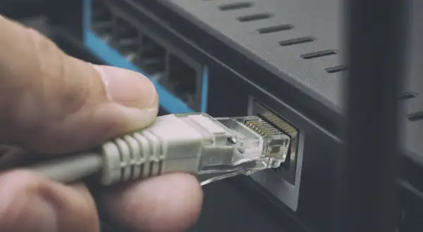 Dłoń podłącza kabel sieciowy kategorii do routera, zapewniając stabilne połączenie internetowe.