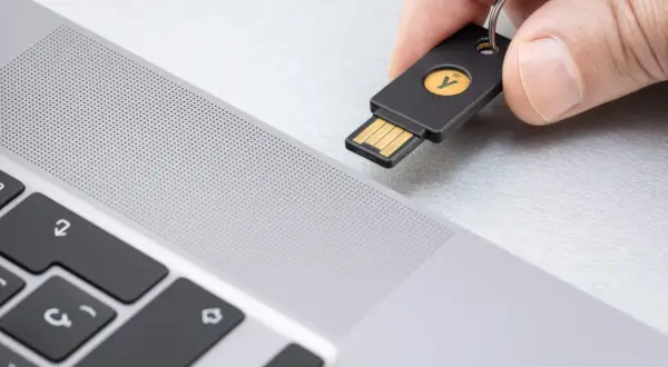 Dłoń zbliża klucz U2F do laptopa. To proste rozwiązanie, które odpowiada na pytanie klucz u2f co to jest – fizyczny klucz do bezpiecznego logowania.