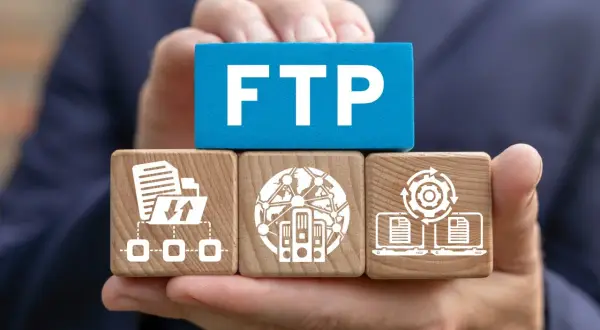 Dłonie trzymają kostki symbolizujące połączenie FTP: transfer plików, serwery w sieci i synchronizację danych.