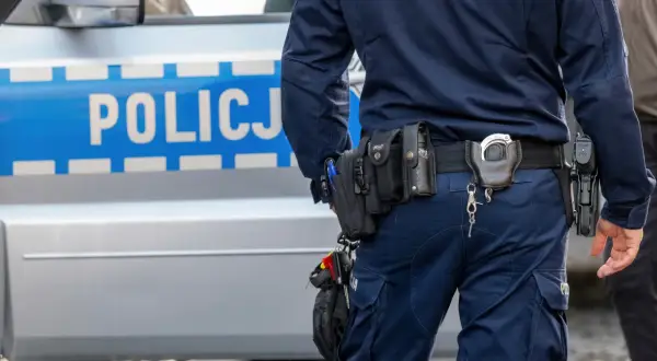 Policjant w pełnym rynsztunku, z pistoletem i kajdankami, stoi obok radiowozu. Wszystko wygląda na rutynową kontrolę, ale czy na pewno? Czasem nawet najbardziej oczywiste sygnały mogą okazać się fałszywym pozytywem.