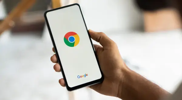 Dłoń trzyma smartfon z logo Chrome. Chcesz wiedzieć, jak usunąć synchronizację Google?