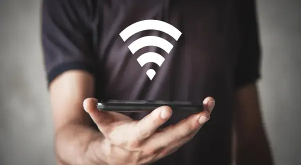 Dłoń trzyma smartfon, nad którym unosi się biały symbol Wi-Fi, symbolizujący szybkie połączenie wi-fi 6e.