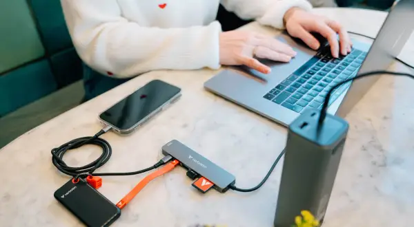 Kobieta pracuje na laptopie, podłączając telefon, dysk zewnętrzny i kartę SD do huba USB 3.2 Gen. 1.