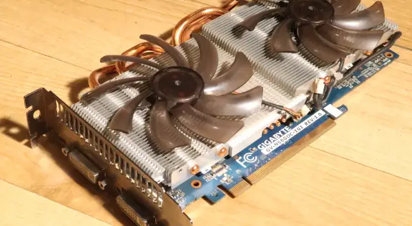 Karta graficzna Gigabyte GTX 560 Ti z dwoma wentylatorami i miedzianymi rurkami cieplnymi na drewnianym tle.