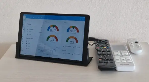 Tablet z systemem Linux wyświetla dane o temperaturze i wilgotności. Obok leżą piloty.