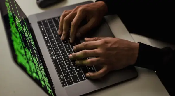 Ręce piszą kod na laptopie, ekran wyświetla zielony tekst. Czy to haker?