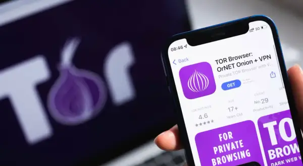 Aplikacja TOR Browser na telefonie, obok logo TOR na ekranie laptopa. Dowiedz się, jak wejść do darknetu, korzystając z tej przeglądarki.
