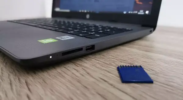 Laptop z czytnikiem kart SD. Obok leży niebieska karta pamięci, która jest zabezpieczona przed zapisem.