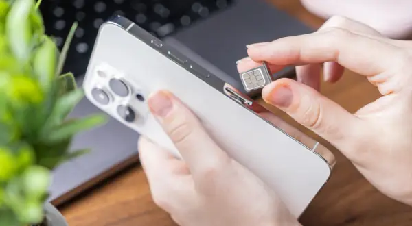 Dłoń wkłada kartę SIM do telefonu, przygotowując się do zmiany operatora lub konfiguracji nowego urządzenia.