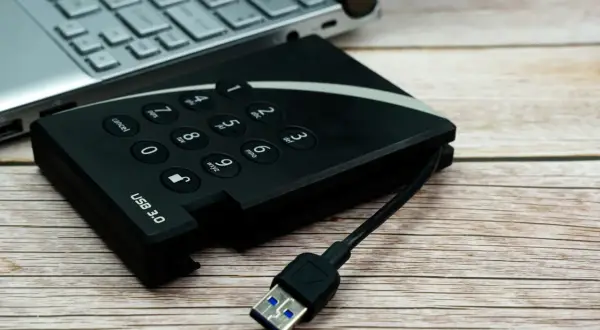 Dysk zewnętrzny z klawiaturą numeryczną i kablem USB 3.0 obok laptopa, gotowy do udostępniania internetu z telefonu na komputer przez USB.