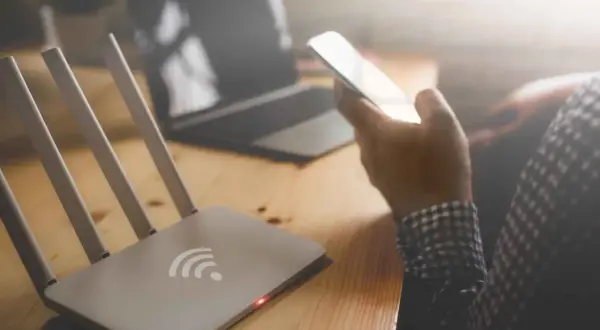 Router i smartfon na biurku. Zastanawiasz się, jak sprawdzić na jakie strony ktoś wchodził wifi?