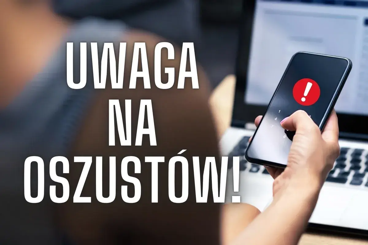 Uważaj na oszustów w internecie! Dłoń z telefonem i ostrzeżeniem na ekranie obok laptopa.