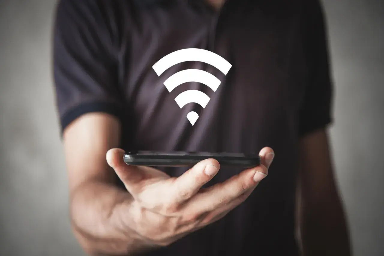Dłoń trzyma smartfon, nad którym unosi się biały symbol Wi-Fi, symbolizujący szybkie połączenie wi-fi 6e.