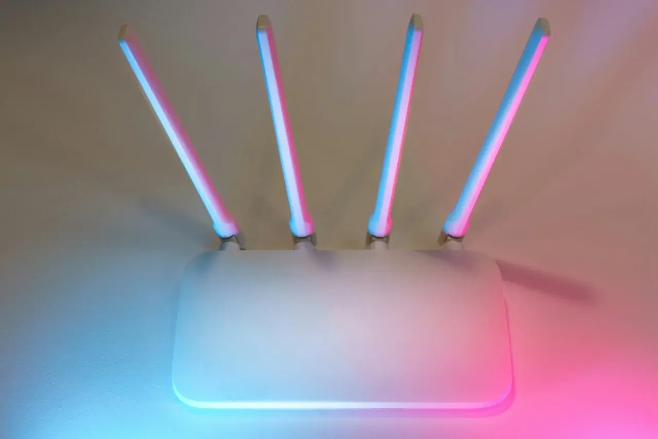 Biały router z czterema antenami, podświetlony na niebiesko i różowo. Kluczowy element zabezpieczenia sieci.