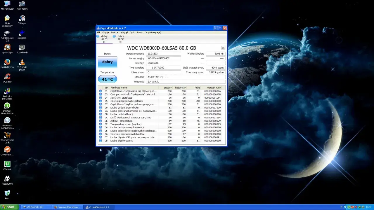 Na pulpicie systemu Windows z tapetą kosmiczną widać okno programu CrystalDiskInfo, który monitoruje stan dysku twardego. W tle, na pasku zadań, widoczny jest skrót do "Linux na starym kompu...", sugerujący, że system ten jest używany.