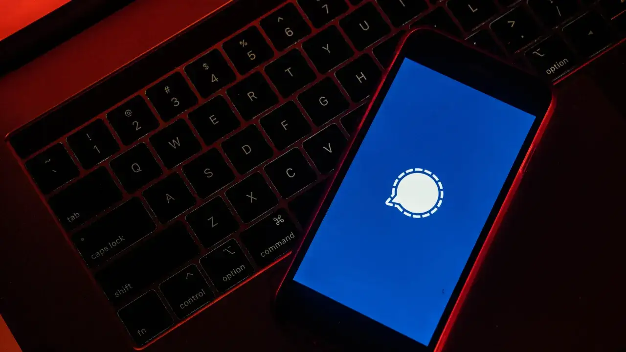 Czerwone światło oświetla klawiaturę laptopa i smartfon z logo Signal. Czy Signal jest bezpieczny? To pytanie nurtuje wielu użytkowników.