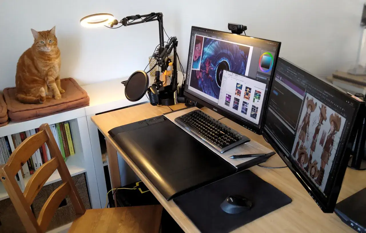 Pomarańczowy kot pilnuje stanowiska do pracy w linux multimedia studio. Na biurku dwa monitory, tablet graficzny, mikrofon i klawiatura.